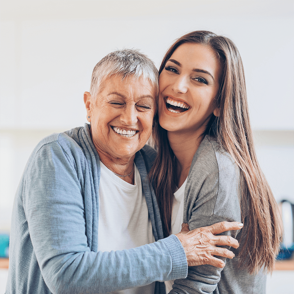 Погрижете се за вашето психично здраве с GenPro На снимката са изобразени възрастна жена и млада жена които са усмихнати и се прегръщат.